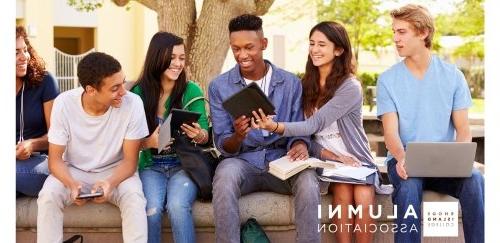 Students sitting outside together on a wall looking at tables, books, materials